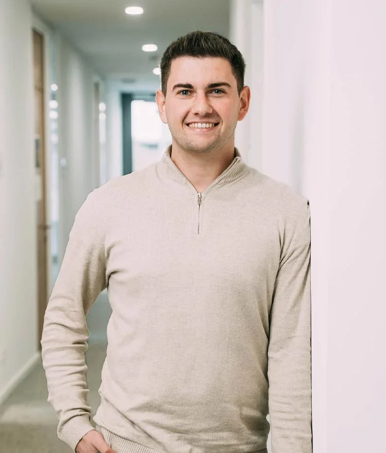 Junger Mann in Beige-Pullover steht lächelnd in einem Flur