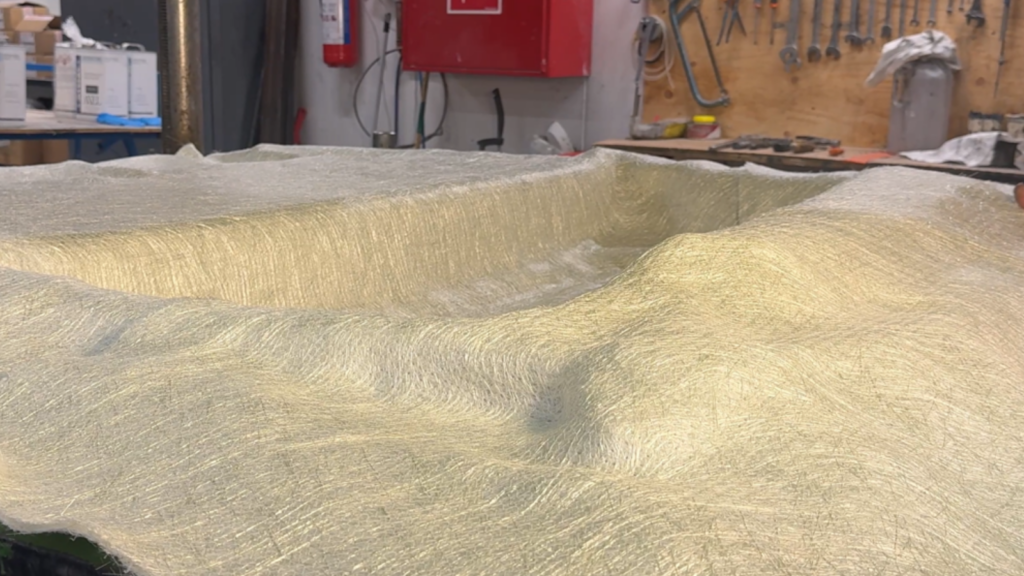 Eine gebogene Materialoberfläche in einer Werkstatt mit Werkzeugen im Hintergrund.