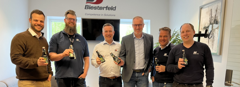 Gruppe von Personen in einem Büro, die Bierflaschen halten.