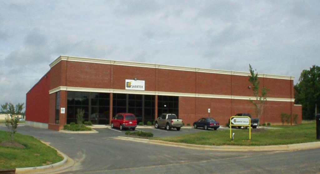 A low, red brick building with several cars parked in front of the entrance.