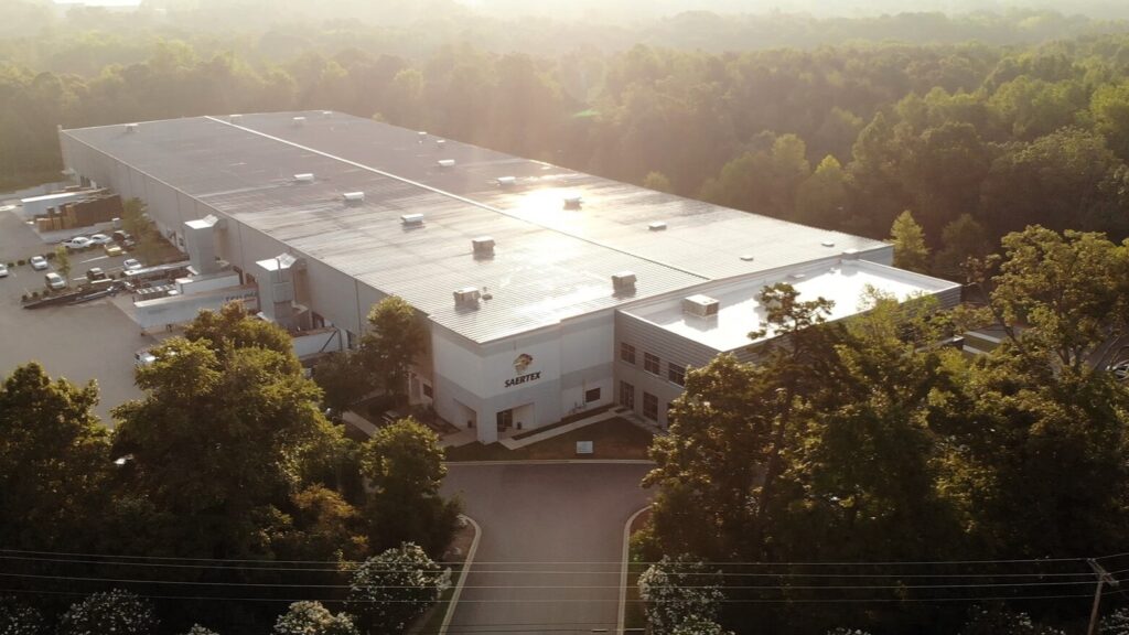 Aerial view of a large industrial building surrounded by trees at sunset.